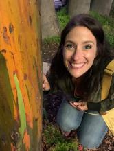 picture of teacher smiling next to a rainbow eucalyptus tree